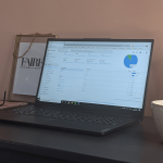 Laptop showing Google Analytics overview on a desk surrounded by a coffee cup, glasses and Faire Marketing's framed logo